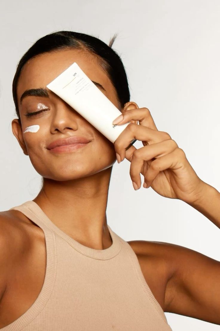 Woman holding a sunscreen tube beside her face with sunscreen on her cheek